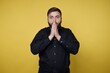 © bodnarphoto - Man stands with hands together and surprised expression in front of bright yellow background
