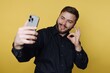 © bodnarphoto - Man taking a selfie and smiling while standing in front of a yellow background in a casual setting