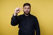 © bodnarphoto - Man gestures with hand to show small size in front of yellow background during indoor session in the afternoon