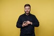 © bodnarphoto - Man using smartphone against yellow background while smiling and engaging with device