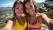 © Maksym - Two happy women friends capturing selfie on hiking trail, wearing colorful sport tops, rugged terrain and distant valley visible, exploring ancient ruins in background, bright sunn