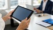 © ng-TDRD - A person holds a tablet in a modern office, with a colleague visible in the background, illustrating technology in a business environment.