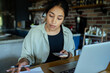 © Marko Geber - Young woman working from home kitchen with laptop and smartphone