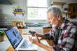 © Marko Geber - Senior man consulting doctor online with inhaler at home kitchen