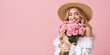 © Milan - Happy woman with straw hat holding pink carnations. Young blonde female with flower bouquet on pink background. Spring celebration concept. Copy space for text