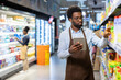 © Liubomir - Retail worker holding a digital tablet while performing inventory management and restocking shelves with products at a grocery store, ensuring efficient store operations