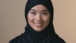 © Yuliia - Smiling Asian Muslim business woman in hijab looking at camera indoor happy executive female professional workplace modern Islamic girl confident toothy smile dental service laughing success career