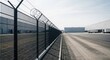 © Hamster - Black security fence topped with barbed wire securing a warehouse area. Industrial perimeter protection and restricted access concept.