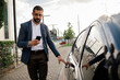 © kleberpicui - Business man using a smartphone while opening a car door on an urban street. Concepts of mobility, modern lifestyle, commuting, technology and daily routine