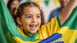 © Photyn Studio - A smiling Brazilian girl holds a flag, cheering for a World Cup soccer match. With family at home