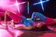 © pressmaster - Caucasian young adult women performing glute bridge exercise on yoga mats in fitness studio, engaging in group workout session under colorful neon lights, wearing athletic outfits