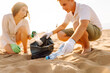 © maxbelchenko - A small group of volunteers cleans the beach of plastic at sunset. Two young women and a man work outdoors and enjoy the seascape. Concepts of ecology and volunteerism.