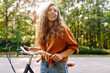 © maxbelchenko - A young woman on a bicycle in a sunny park. A cheerful tourist rides a bicycle outdoors, enjoying nature. Concept: transportation, leisure, active lifestyle.