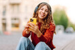 © maxbelchenko - A cheerful woman with wireless headphones and a phone enjoys the urban environment on a sunny day. A young woman listens to music and strolls through the old town. Concept of rest and relaxation.