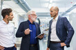 © Westend61 - Senior male manager with colleagues discussing over digital tablet while standing at illuminated factory