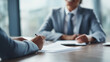 © Broccolini - Professional financial consultation scene with two business people discussing documents across a desk, featuring a laptop and a pen in a modern office.