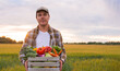 © Acronym - Farmer with a vegetable box in front of a sunset agricultural landscape. Man in a countryside field. Country life, food production, farming and country lifestyle concept.