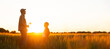 © Acronym - Farmer and his son in front of a sunset agricultural landscape. Man and a boy in a countryside field. Fatherhood, country life, farming and country lifestyle concept.