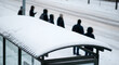 © val_webart - People waiting at a snowy bus stop during winter in a city