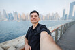 © Studio Peace - Man taking selfie with the cityscape in the background. Traveler enjoying city travel and urban exploration. Tourism concept.
