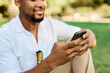 © Lumos sp - Young man enjoys sunny day while using smartphone in park, highlighting his joy and connection to the world around him