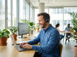 © Md Ikbal - A man wearing a headset works on a laptop at a desk in a modern office with large windows and plants