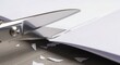 © Nataly - Close-up of silver scissors cutting white paper. Office or craft supplies on a wooden desk. Precision work concept
