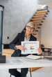 © Novak - Confident middle-aged businesswoman in a blue suit showing financial results to the camera.