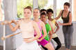 © JackF - Fit girl practicing at barre with group of teenage ballet students, learning demi plie under guidance of female instructor in mirrored hall of choreography studio..