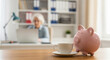 © ViskBx - Senior woman working on laptop with piggy bank and coffee cup on desk
