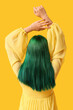 © Pixel-Shot - Young woman with green hair on yellow background, back view