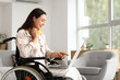 © Pixel-Shot - Young woman in wheelchair using laptop at home