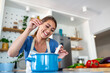© Graphicroyalty - Smiling woman in kitchen wearing apron seasoning blue pot with salt while cooking healthy meal. Happy female chef preparing dinner with fresh vegetables on counter. Home culinary and nutrition theme.