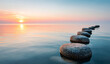 © Selvi - Row of smooth, rounded stones with textured surfaces extending into calm water during sunset, creating a peaceful and scenic landscape