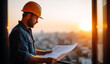 © andyaziz6 - Male construction engineer wearing orange hard hat and denim shirt reviewing blueprints during sunset at a building site