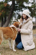© SHOTPRIME STUDIO - Dog and woman share a gentle moment in a pale winter coat, kneeling on grass as they connect in a park setting, showcasing companionship, care, calm outdoor bonding, warm textures, and mindful