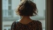 © Anastasiia - Back view of a person with short brown hair in a blue floral dress, standing by a window overlooking buildings. Concept Back view portrait, Short brown hair, Blue floral dress, Standing by a window