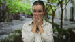 © Krakenimages.com - Woman covering mouth with both hands against an urban sidewalk lined with green trees on a sunny morning; gratitude.