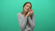 © Krakenimages.com - Woman holding red apple to cheek in studio with teal green background, eyes closed and gentle smile while embracing the fruit; contentment affection.