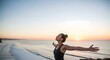 © Widdy - A woman stretches her arms wide while standing by the sea at sunrise, embracing freedom, positivity, and fresh ocean air.