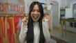 © Krakenimages.com - Young chinese woman smiling in indoor clothing shop with colorful outfits in background showcasing retail fashion.