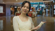 © Krakenimages.com - Woman presenting indoors at a modern mall shop center with a friendly smile, highlighting store ambiance in a bustling retail environment.