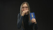 © Krakenimages.com - Woman holding ukraine passport with hand covering mouth while laughing and showing passport front in studio black backdrop; joy travel.