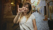 © Krakenimages.com - Woman smiling holds pinky finger up in a narrow cobblestone street with fountain and storefronts in view; playful promise.