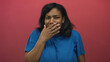 © Krakenimages.com - African american woman wearing blue t shirt covers mouth with hand in studio with red wall; disgust.
