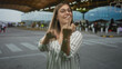 © Krakenimages.com - Blonde woman flashing middle finger and miming a crank motion outside an airport terminal arrivals area; defiance insult.