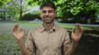 © Krakenimages.com - Young hispanic man holding open palms standing in a green park with lush foliage; welcoming serenity.