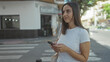 © Krakenimages.com - Woman holds phone with both hands, texting while standing on a crosswalk street in an urban downtown wearing white tshirt and smiling; calm concentration.