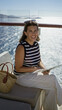 © Krakenimages.com - Woman seated on a cruise terrace reading a brochure with straw bag and sunglasses nearby by the glass railing building; serene escape.