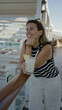 © Krakenimages.com - Woman leaning on railing with cocktail and hand on chin on ship terrace wearing striped top and sunglasses on head; relaxation vacation escape.